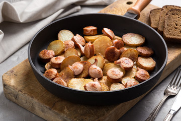 Close-up shot of fried potatoes with sausages and egg. Breakfast. Potatoes with sausages, cut into slices and fried in oil, in rustic style. Frying pan with tasty cooked egg and sausages on table