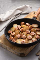 Close-up shot of fried potatoes with sausages and egg. Breakfast. Potatoes with sausages, cut into slices and fried in oil, in rustic style. Frying pan with tasty cooked egg and sausages on table