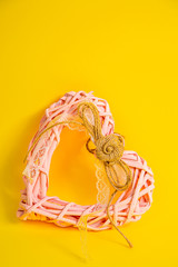 Pink heart made of wooden branches with a bow made of thread. Valentine's Day. yellow background. 