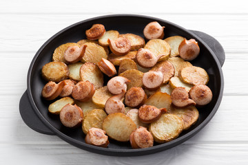 Close-up shot of fried potatoes with sausages and egg. Breakfast. Potatoes with sausages, cut into slices and fried in oil, in rustic style. Frying pan with tasty cooked egg and sausages on table