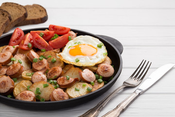 Close-up shot of fried potatoes with sausages and egg. Breakfast. Potatoes with sausages, cut into slices and fried in oil, in rustic style. Frying pan with tasty cooked egg and sausages on table