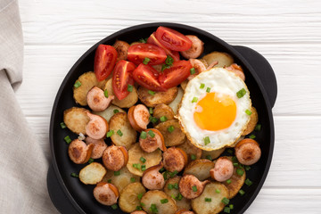 Close-up shot of fried potatoes with sausages and egg. Breakfast. Potatoes with sausages, cut into slices and fried in oil, in rustic style. Frying pan with tasty cooked egg and sausages on table
