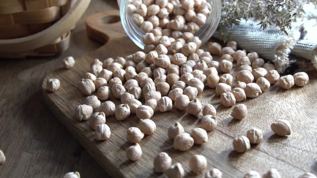 Dried uncooked chickpeas falling in slow motion over the table from a jar. Vegetarian food packed with minerals, iron, magnesium, pottasium and other minerals. Healthy source of fiber.