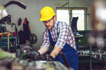 Turner worker is working on a lathe machine in a factory.  