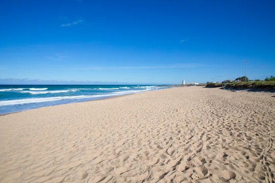 scenery of beautiful and lonely Palmar Beach with sand, turquoise ocean water and ancient tower in the horizon. In Vejer village (Cadiz, Andalusia, Spain)