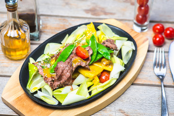Fried pieces of meat with vegetables in a hot pan on a wooden table in a restaurant.