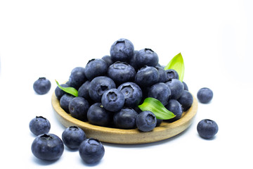 Blueberries on a wooden plate with green leaves on a white background