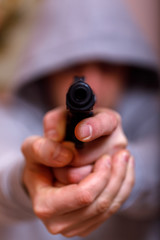 Man in hood with gun or pistol. Gangster, violence, outrage, force, rape or criminal concept, focus on the gun.