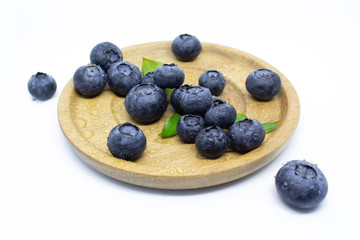 Blueberries on a wooden plate with green leaves on a white background