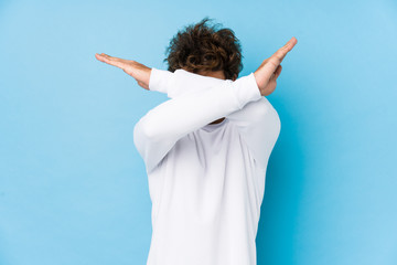 Young caucasian man against a blue background isolated keeping two arms crossed, denial concept.