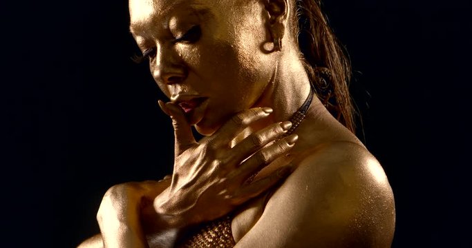 alluring black woman is painted golden dye, stroking her shoulders and breasts