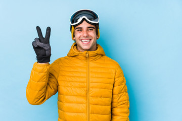 Young skier man wearing snowboard goggles isolated joyful and carefree showing a peace symbol with fingers.