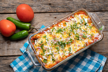 Mexican red baked enchiladas with melted cheese and sour cream on wooden background