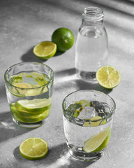 Water fitness detox with lime on a light grey background. Hard sun light and shadow. Soda coctail