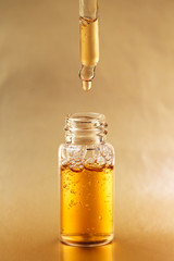 Bottle of cosmetic oil with pipette on golden background. Front view.