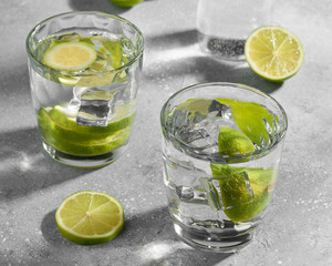Water fitness detox with lime on a light grey background. Hard sun light and shadow. Soda coctail