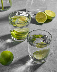 Water fitness detox with lime on a light grey background. Hard sun light and shadow. Soda coctail