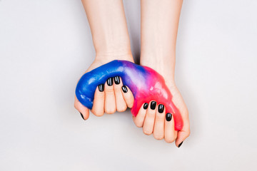 hands with black manicure holding slime in blue and pink vibrant colors