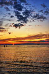 Beautiful sunset on the Baltic Sea beach. People walk in the water and a ship sails in the background.