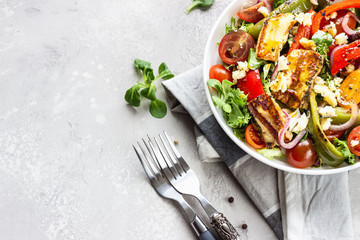 Vegetable salad cherry tomatoes, baked pepper, salad mix and onion with grilled haloumi (halloumi) cheese. Keto diet, healthy food. Light grey stone background. Top view.
