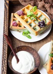 Traditional Belgian waffles with frozen berries, mint and natural greek yogurt on a plate in a wooden tray. Breakfast. Top view.