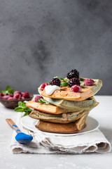 A stack of homemade Belgian waffles with frozen berries, mint and natural greek yogurt on a white plate, light grey stone background. 
