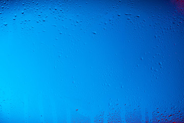 Glass with water drops on colorful background.