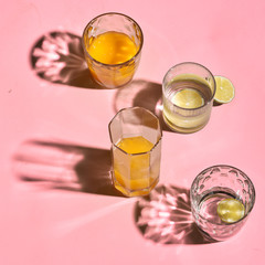 glass with orange juice on bright pink background.  Sun hard light shadow reflection. Tropical summer minimalism concept