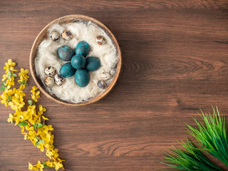 Colorful Easter eggs in nest and spring flowers on wooden table. Easter holiday decorations , Easter concept background.
