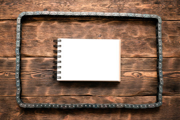 Car fix list template. Valve train chain and blank page notepad on brown wooden workbench flat lay background.