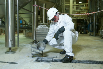 factory worker in personal protective equipment inspecting floor drain in the manufacturing facility
