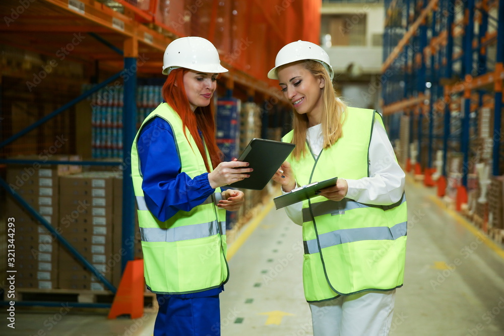 Wall mural warehouse staff discuss warehouse processes. two women warehouse workers on the background of orange shelves with goods