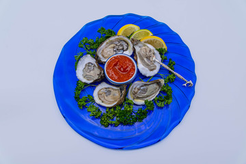 Oysters on the half-shell served on a round, blue glass plate with cocktail sauce and an ornate cocktail fork.