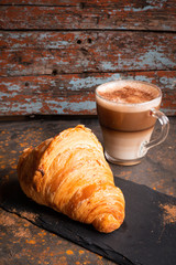 Crisp chocolate croissant based on the dark plate with cappuccino