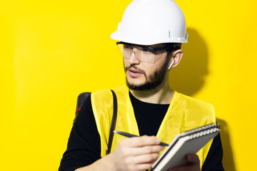 Studio portrait of young confident man, builder engineer writing in notebook, using wireless...