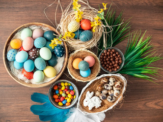 Colorful Easter eggs in nest, feathers and spring flowers on wooden table. Easter holiday decorations , Easter concept background.