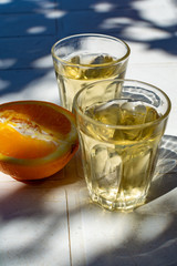 Greek wine in 2 glasses, fresh ripe orange served in garden in sun lights