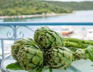 Fototapeta premium Cooking with fresh green artichokes heads, tasty vegetarian food, on open kitchen with sea view