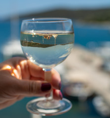 Woman hand with one glass of wine and blue sea view