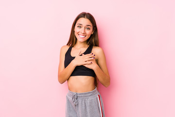 Young caucasian fitness woman posing in a pink background has friendly expression, pressing palm to chest. Love concept.