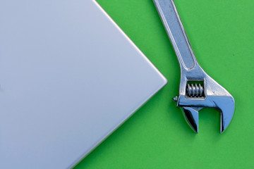 Adjustable wrench next to a silver laptop. Computer service, maintenance theme.