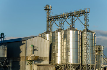 A large modern plant for the storage and processing of grain crops. view of the granary on a sunny day. Large iron barrels of grain against the sky. End of harvest season.