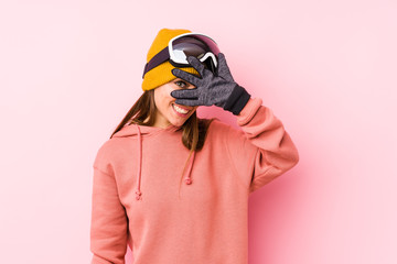 Young caucasian woman wearing a ski clothes isolated blink at the camera through fingers, embarrassed covering face.