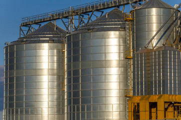 A large modern plant for the storage and processing of grain crops. view of the granary on a sunny day. Large iron barrels of grain against the sky. End of harvest season.
