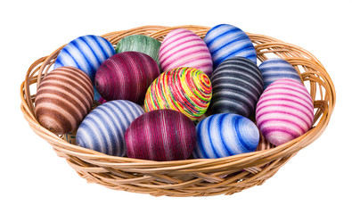 Colorful ornate Easter eggs pile in wicker basket isolated on white background. Hand-decorated striped egg shells wrapped by glued thin cotton sewing yarn. Ornate empty eggshells. Full depth of field.