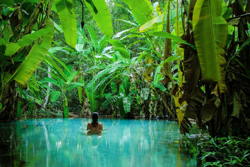 A girl stands in a natural pool surrounded by banana tree's leafs