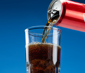 Carbonated drink pours from an aluminum can into a glass