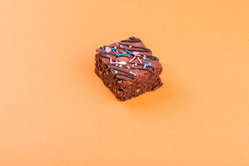 Chocolate brownie dessert with almond nut, chocolate glaze on an orange background.
