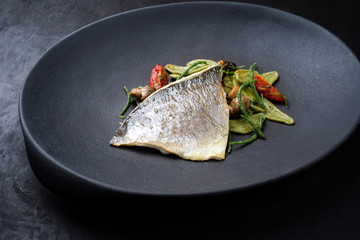 Gourmet fried Italian gilthead fish filet with spinach pasta, glasswort and tomatoes as closeup on a modern design plate