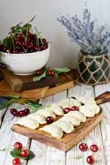 Juicy dumplings with fresh cherries on a wooden cutting board. An image of raw dumplings with fresh cherries on a white rustic table. Rustic. A national dish. Top view.